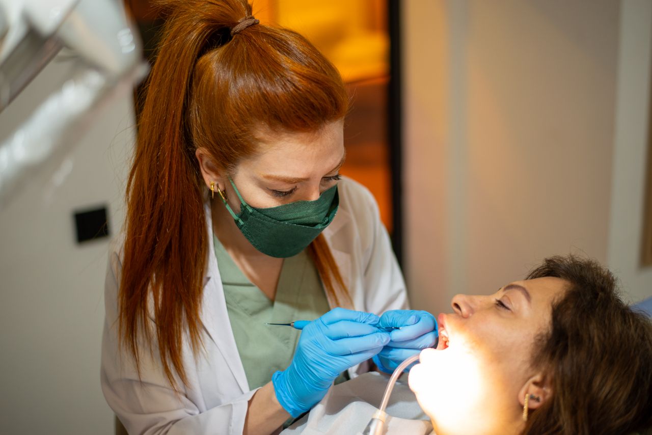 Female dentist wearing protective gear examines a patient in a dental clinic.