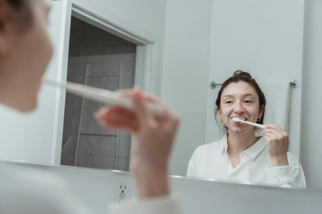 Home A woman with hair bun brushing her teeth in front of mirror, focusing on dental hygiene.