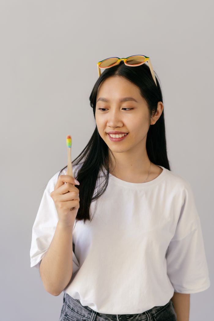 Home Asian woman smiling and holding a rainbow-colored toothbrush, indoors.
