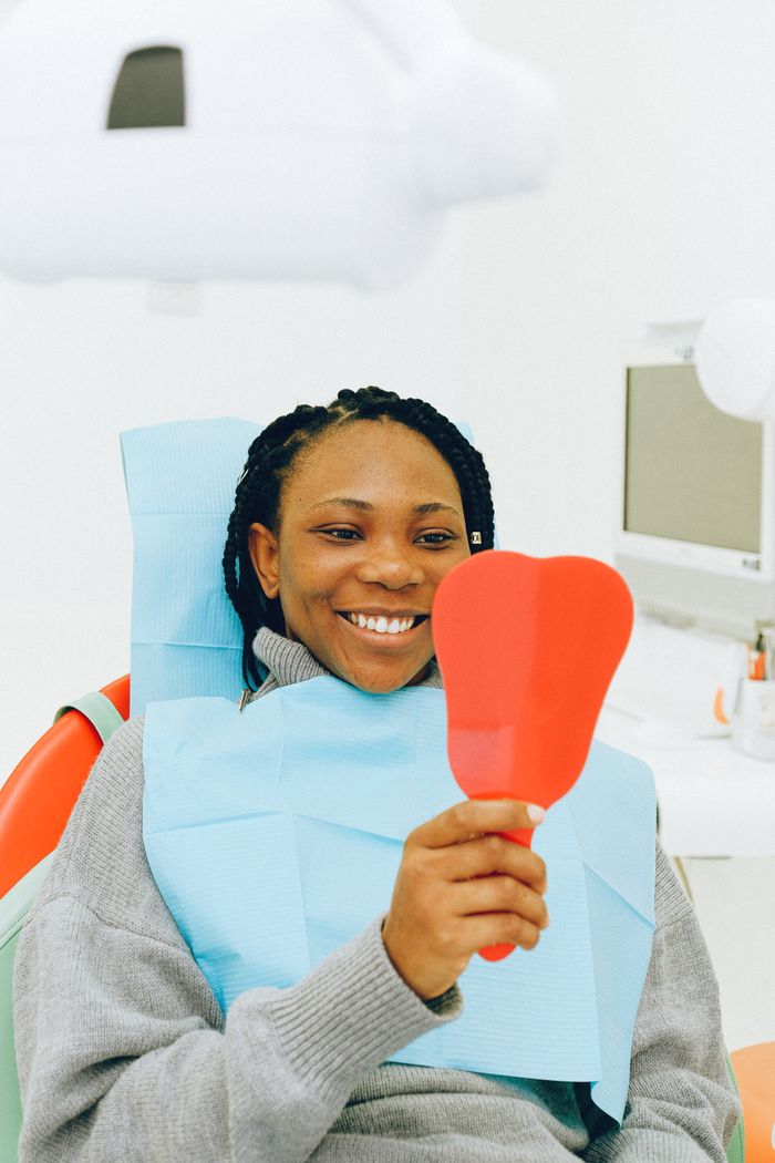 Home Smiling woman in a dental clinic holding a mirror, showcasing her bright smile.