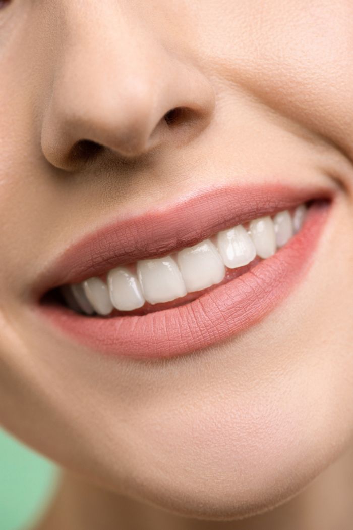 A close-up image focusing on a womans smiling mouth, showing white teeth and pink lips.